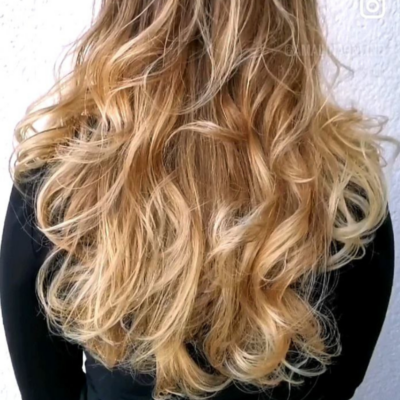 Nahaufnahme von langem, welligem blondem Haar, professionell gestylt in weichen, voluminösen Locken mit natürlichem Glanz und Bewegung
