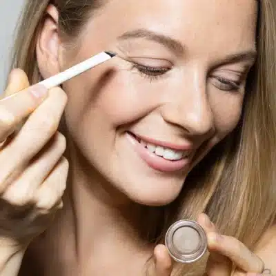 Frau trägt Uoga Uoga Eyebrow Pomade mit einem abgeschrägten Pinsel auf ihre Augenbraue auf